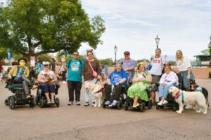 A group of people including five service dogs and five wheelchair users pose together at Disney World.